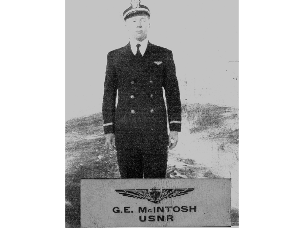 Charlie Danaher In May 2025 Cold Facts: 'A Salute To An Old Friend, Glen Mcintosh' 4 A black-and-white photo of a person in a naval uniform with a peaked cap, standing in front of a sign that reads "g. E. Mcintosh usnr" with a naval insignia above the text. The background is blurred, suggesting an outdoor setting.